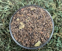 a small bowl of black and brown powder on top of green grass