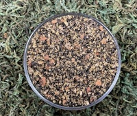 a small bowl of brown and black granules on top of green grass